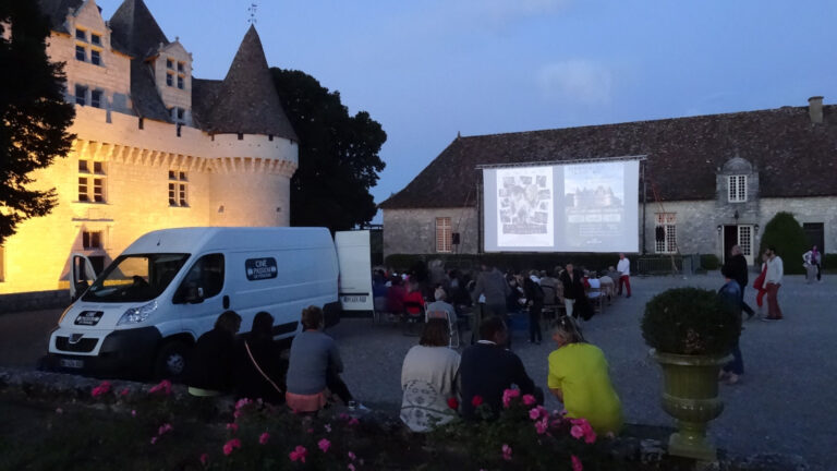 Devant un chateau, des personnes regardent un écran : c'est une séance de cinéma itinérant en plein air.
